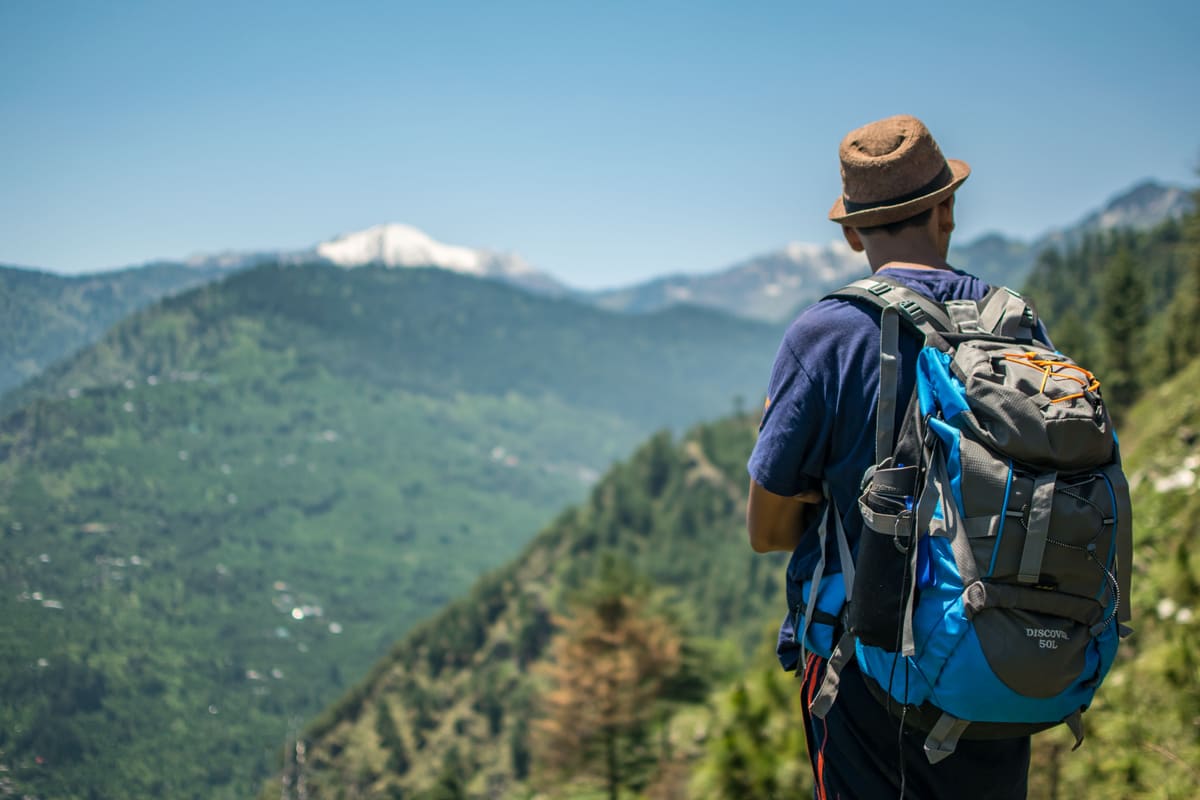 Man with backpack hiking among green mountains under clear blue sky.